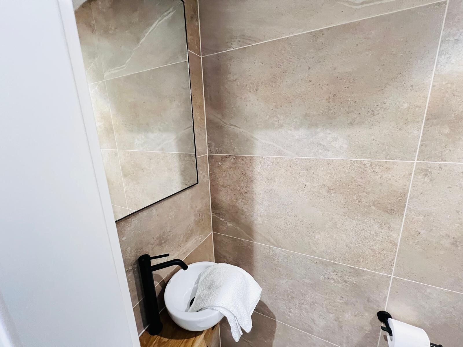 A bathroom with beige tiles, a white sink, and a black towel rack.