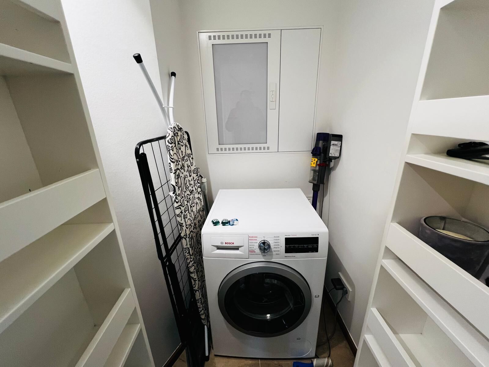 A compact laundry room with a Bosch washing machine, a drying rack, and a wall-mounted control panel.