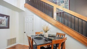 Un área de comedor con una escalera de madera, una puerta blanca y un cuadro en la pared.