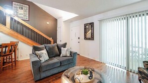 Una sala de estar con un sofá gris, una mesa de comedor de madera y una escalera.