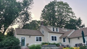 A two-story house with a front porch, a stone retaining wall, and a well-maintained garden with various flowers and shrubs. - Antique farmhouse with spectacular mountain view in a bucolic setting. (West Windsor)