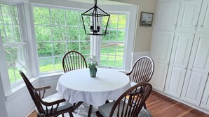A dining area with a round table, four wooden chairs, a white tablecloth, a vase with flowers, and a hanging light fixture. - Antique farmhouse with spectacular mountain view in a bucolic setting. (West Windsor)