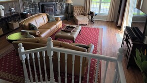A living room with a stone fireplace, leather sofas, a red patterned rug, and a large window with curtains. - Antique farmhouse with spectacular mountain view in a bucolic setting. (West Windsor)