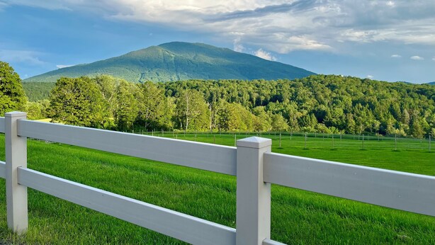 A white fence in a lush green field with a mountain in the background. - Antique farmhouse with spectacular mountain view in a bucolic setting. (West Windsor)