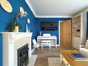 A living room with a fireplace, a piano, a television, and a bookshelf. - NEW Cosy 2 Bedroom Home | Free Parking + Garden (Canterbury)