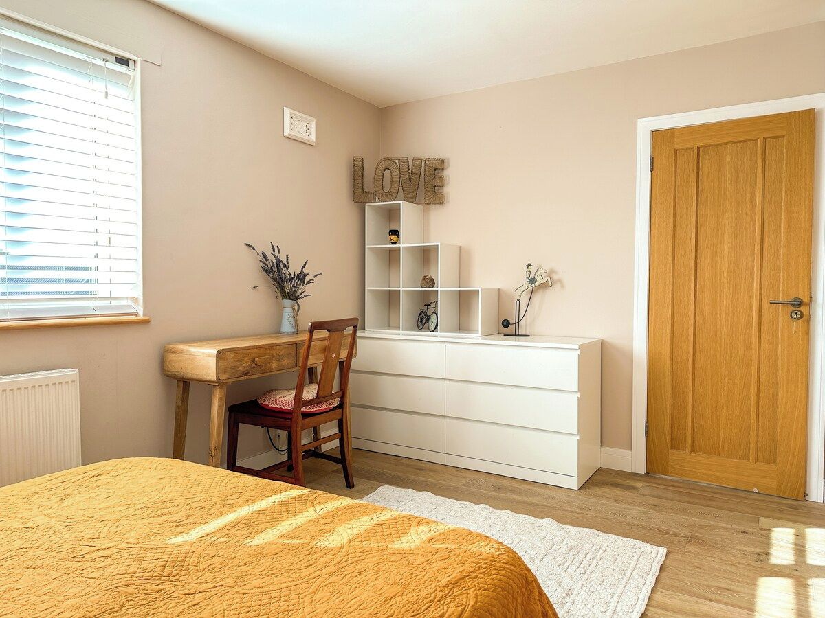 Une chambre à coucher avec un lit, un bureau, une chaise, une commode et une porte.