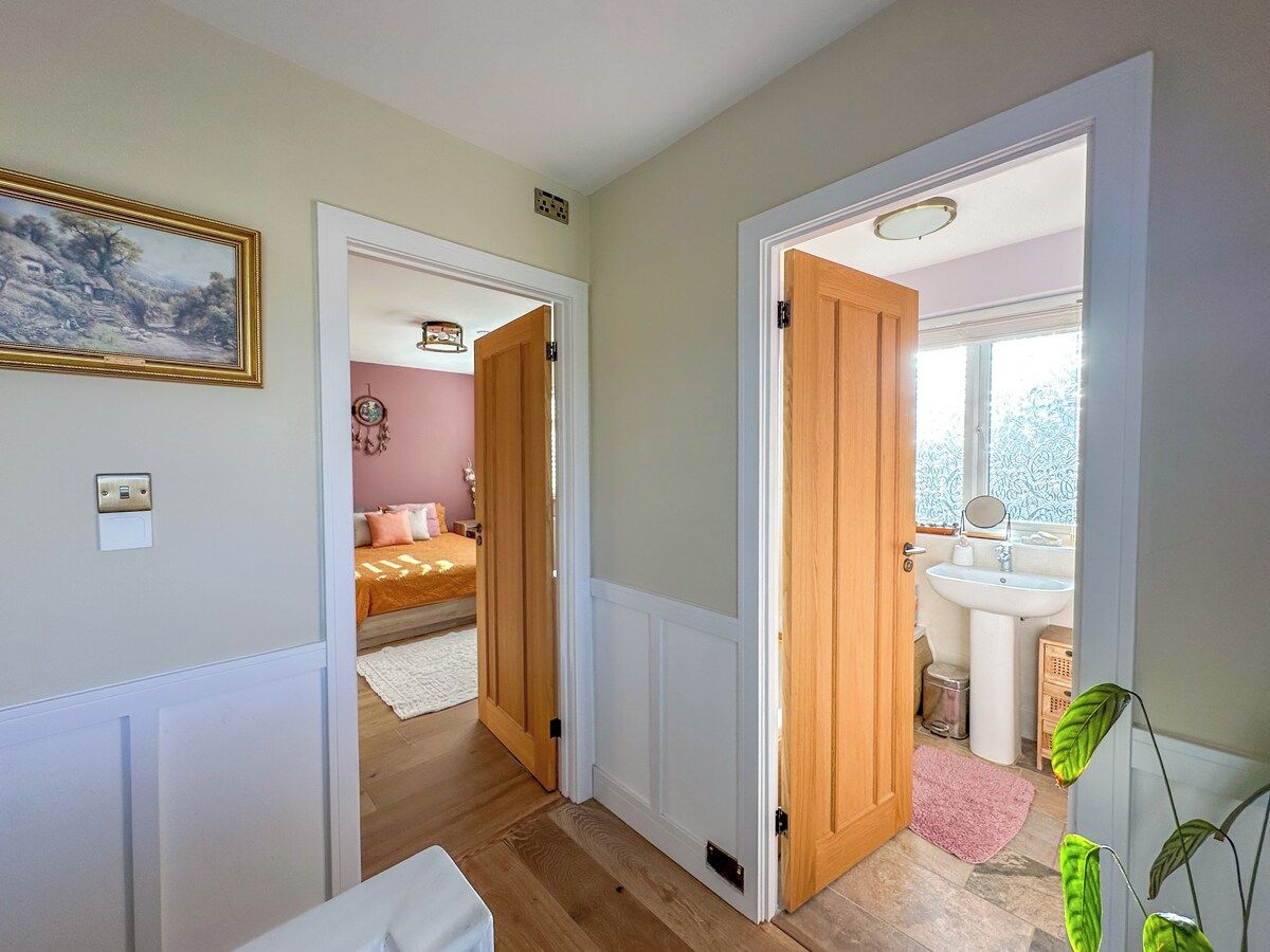 A hallway leading to a bedroom and bathroom with wooden doors, a painting on the wall, and a plant.