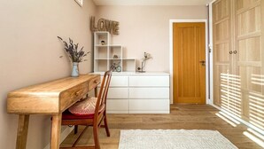 Un couloir avec un bureau en bois, une chaise, une commode blanche et une porte.