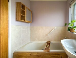 A bathroom with a wooden bathtub, a wooden vanity, a mirror, and a window with a plant.