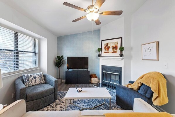 A living room with a ceiling fan, a fireplace, a flat-screen TV, and a sofa. - Charming Private Oasis - close to airport, mall, and downtown. (Raleigh)