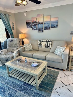 A living room with a sofa, armchair, coffee table, and artwork on the wall.