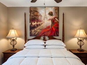 A hotel room with a large bed, two bedside tables with lamps, and a painting of a cityscape.
