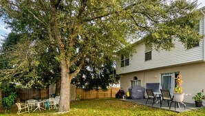 Un giardino con un albero, un barbecue e mobili da esterno.