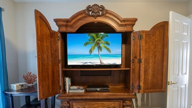 Un mobile in legno contenente un centro di intrattenimento con televisore che mostra una spiaggia, un tavolino con libri e una sedia.