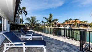 A poolside area with lounge chairs and a view of a marina. - Waterfront home (Marco Island)