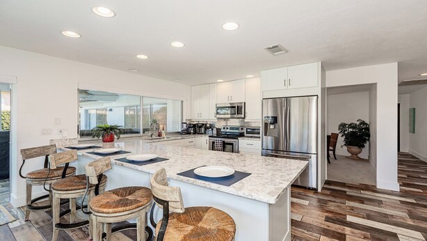 A modern kitchen with white cabinetry, a large island with bar stools, stainless steel appliances, and a view to the outside. - Waterfront home (Marco Island)