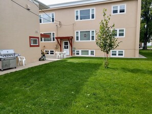 A residential building with a well-maintained lawn, a barbecue grill, and outdoor seating.