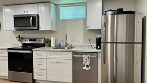 Eine moderne Küche mit weißen Schränken, Edelstahlgeräten, einer eingebauten Mikrowelle, einem Backofen, einem Geschirrspüler und einem Kühlschrank.