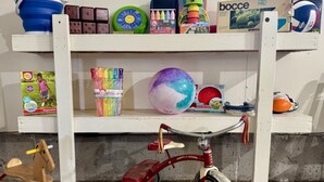 Une étagère remplie de jouets pour enfants, notamment un tricycle rouge, un cheval à bascule en bois et diverses balles colorées.
