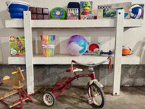 Une étagère remplie de jouets pour enfants, notamment un tricycle rouge, un cheval à bascule en bois et diverses balles colorées.