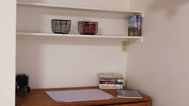 Un petit bureau compact, doté d’un bureau en bois, d’une chaise et d’une étagère contenant des livres et des objets décoratifs.