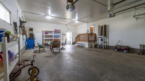 A spacious indoor area with a concrete floor, a wooden staircase, and various items like a bicycle, a toy car, and shelves with objects.