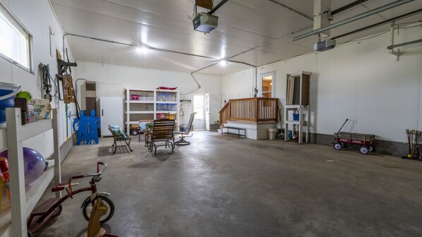 A spacious indoor area with a concrete floor, a wooden staircase, and various items like a bicycle, a toy car, and shelves with objects.