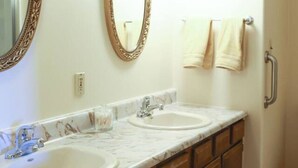 Une salle de bain avec deux lavabos, des meubles en bois, un comptoir en marbre, un grand miroir et un porte-serviettes.