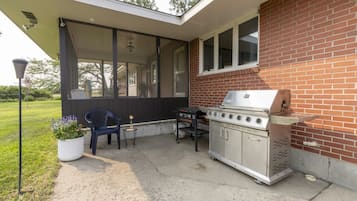 An outdoor patio with a grill, a chair, and a potted plant.