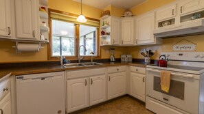 A kitchen with white cabinets, a sink, a stove, and a window with blinds.