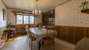Un coin repas avec une table dressée pour six personnes, des chaises en bois, un lustre et une fenêtre donnant sur un beau paysage.