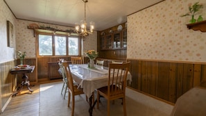 Un coin repas avec une table dressée pour six personnes, des chaises en bois, un lustre et une fenêtre donnant sur un beau paysage.