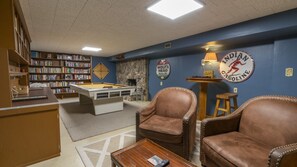 A room with a pool table, leather chairs, a bookshelf, and a wall clock.