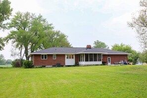 A charming single-story home with a gabled roof and inviting front porch, set amidst a lush lawn and mature trees.