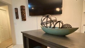 A dining area with a table, two chairs, a bowl with decorative items, a flat-screen TV mounted on the wall, and a chandelier. - Near Manatees, Springs, Scalloping, & Black Diamond (Lecanto)