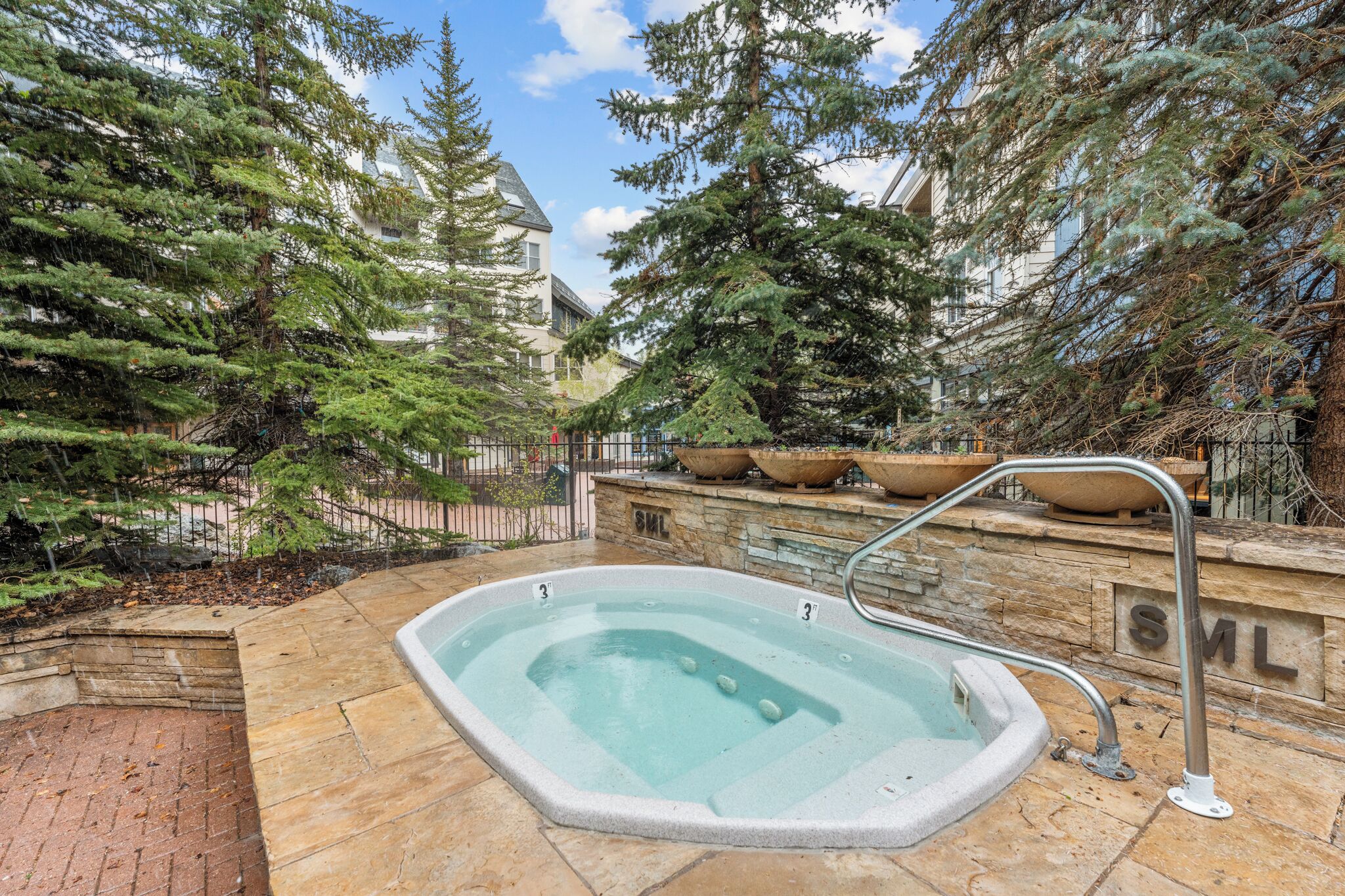 A hot tub surrounded by stone walls and potted plants, with a stone pathway leading to it.