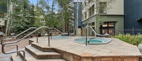 Ett poolområde med trappsteg som leder ner till poolen, omgivet av träd och en byggnad.