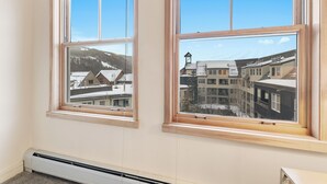 A room with two windows, a wall-mounted heater, and a view of buildings and mountains. - Sm8309-1 (Keystone)