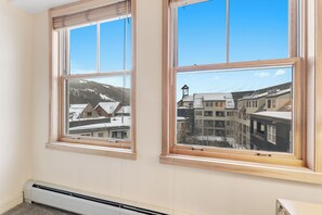 A room with two windows, a wall-mounted heater, and a view of buildings and mountains. - Sm8309-1 (Keystone)