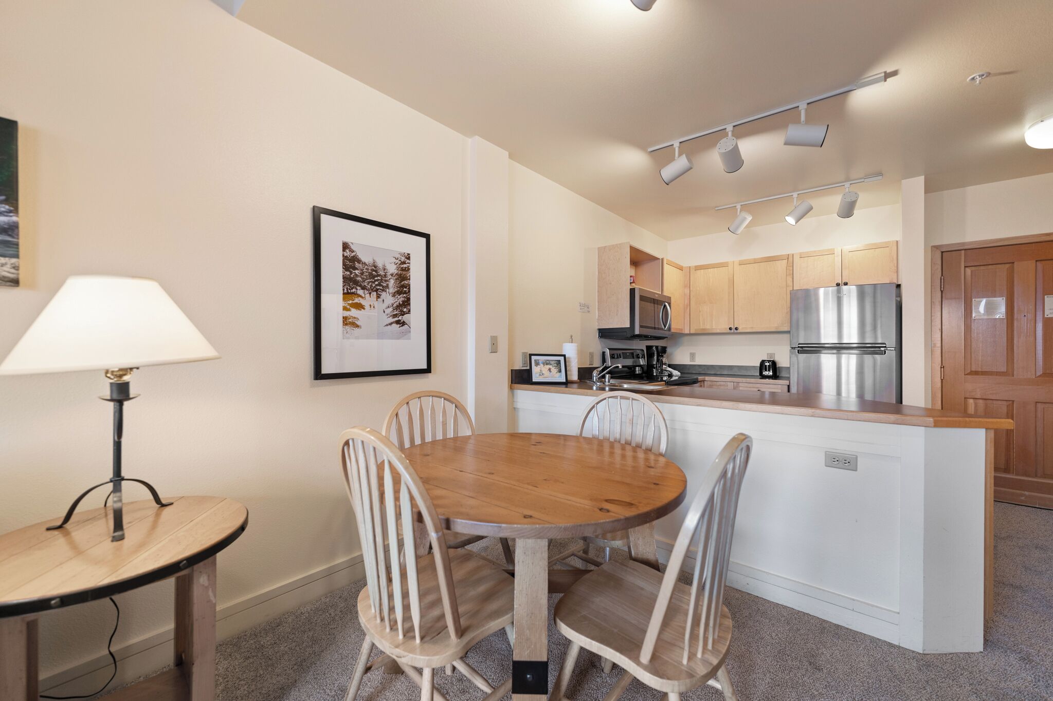 Een moderne keuken met een centraal eiland, houten stoelen, een eettafel en een lamp.