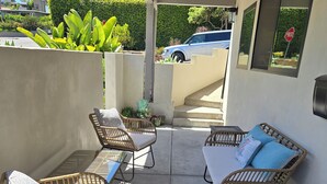 Eine überdachte Terrasse mit Korbmöbeln, einer Fußmatte und Blick auf eine Wohnstraße.