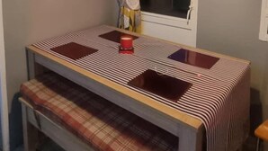 Een kamer met een houten bank, een tafel met een geruite tafelkleed, een raam met gordijn en een hanglamp.