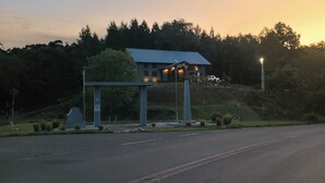 Un área de descanso al borde de la carretera con un refugio cubierto, un banco y un pequeño monumento.