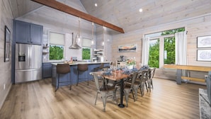 A modern kitchen with a central island, stainless steel appliances, and a dining area with a wooden table and chairs. - Unique Luxury Cabin with swimming pool, outdoor sauna, fire pit, and amazing tree top views! (Broken Bow)