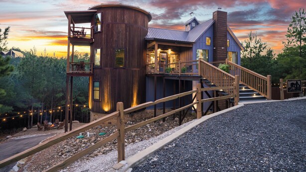 A rustic cabin with a wooden exterior, a balcony, and a staircase leading to the main entrance. - Unique Luxury Cabin with swimming pool, outdoor sauna, fire pit, and amazing tree top views! (Broken Bow)