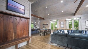 A spacious living area with a wooden bench, a large sofa, a dining table, and a kitchen in the background. - Unique Luxury Cabin with swimming pool, outdoor sauna, fire pit, and amazing tree top views! (Broken Bow)
