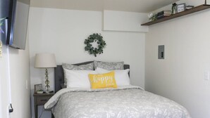 Una cama bien tendida con una colcha de estampado floral y una almohada con la leyenda 'lugar feliz'.