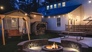 A backyard with a fire pit, a swing set, a covered seating area, and a wooden shed.