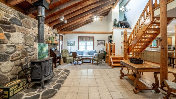A rustic interior with a stone wall, a wood-burning stove, a wooden staircase, and a cozy seating area.