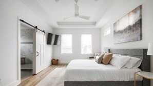 A bedroom with a bed, a ceiling fan, a TV mounted on the wall, and a large window. - The Linden Home - Fountain Square Indianapolis (Indianapolis)